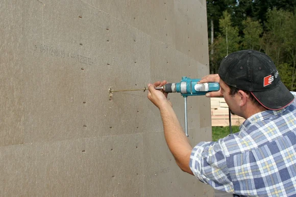 Person befestigt Dämmung an Hauswand mit Bohrmaschine
